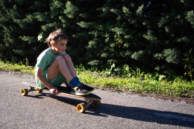 Güneşli bir günün tadını çıkaran çocuk, çitin yanında uzun tahtasında oturuyor.