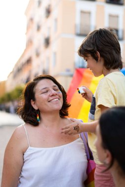 Yüzünde gökkuşağı makyajı olan mutlu bir anne. Gurur yürüyüşü sırasında çocuğu tarafından boyanmış.