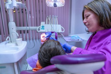 Modern diş sağlığı kliniğinde genç bir hastaya diş kontrolü yapan kadın dişçi.