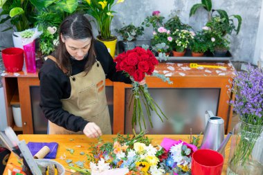Çiçekçide kırmızı güller ve diğer çiçekler düzenleyen bir çiçekçi.