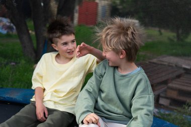 İki neşeli çocuk trambolinde oturuyor, birlikte vakit geçiriyorlar ve bir anlık neşeyi paylaşıyorlar.