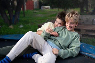 İki kardeş trambolinde yatıyor, arka bahçelerinde sarılıp gülüyorlar.