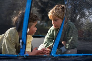 İki kardeş arka bahçelerinde trambolinde dinlenirken sohbet ediyorlar.