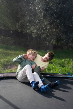 İki kardeş trambolinde eğleniyor ve birlikte oynuyorlar. Bahçede boş vakitlerinin tadını çıkarıyorlar.