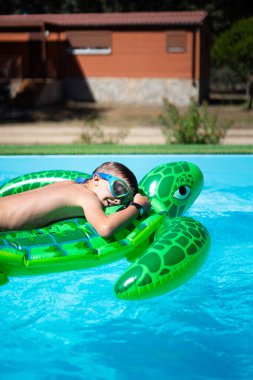 Gözlüklü genç yaz tatilinde şişme yeşil kaplumbağa yüzme havuzunda dinleniyor.