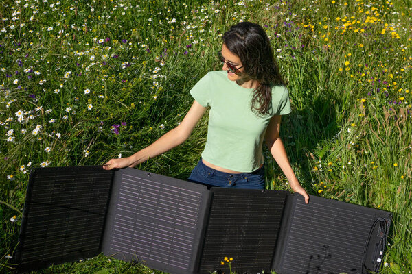 Woman installing a portable solar panel in a wildflower meadow, embracing sustainable energy solutions