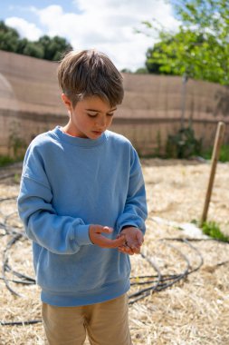 Çocuk çiftçisi elinde bir solucanı analiz ederek sürdürülebilir tarım ve çevre bilincini teşvik ediyor.