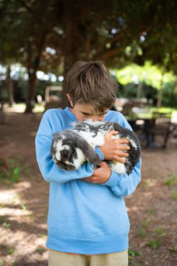 Genç çocuk bir tavşanı sevgiyle tutuyor, dışarıda huzurlu bir anın tadını çıkarıyor.