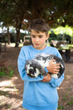 Çocuk bir çiftlik ortamında tavşanı nazikçe kucaklıyor, doğayla iç açıcı bir bağ gösteriyor.