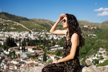 Granada şehrinin manzarasına bakarken gözlerini güneşten koruyan genç bir kadın.