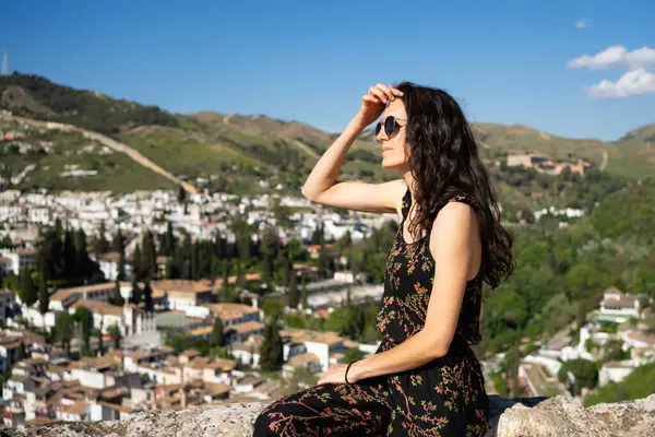 Granada şehrinin manzarasına bakarken gözlerini güneşten koruyan genç bir kadın.