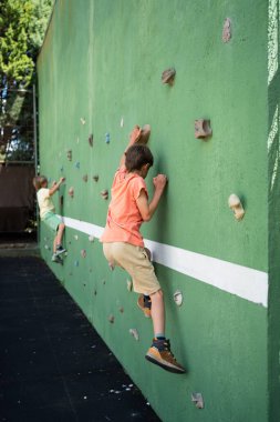 Oyun parkındaki yapay bir duvarda kaya tırmanışı yapan iki çocuk.