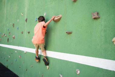 Genç bir çocuk tırmanma duvarında kaya çalışması yapıyor. Güç ve çeviklik kazanıyor.