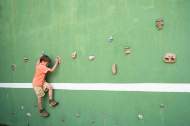Çocuk tırmanma duvarında kayalardan hoşlanıyor, egzersiz yaparken eğleniyor.