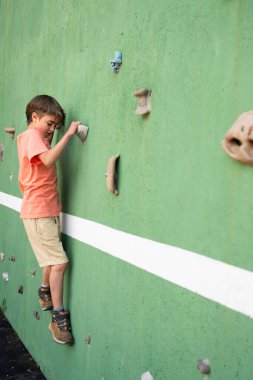 Çocuk tırmanışçı yapay tırmanma duvarında pratik yapıyor, güç ve koordinasyon geliştiriyor.