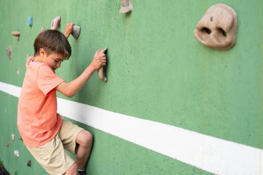 Çocuk tırmanma duvarında pratik yapıyor, güç ve problem çözme becerileri geliştiriyor.