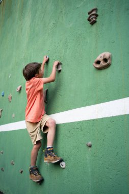Çocuk yapay tırmanma duvarında kaya çalışması yapıyor, sağlıklı aktif yaşam tarzının tadını çıkarıyor.