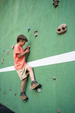 Yapay duvarda kaya tırmanışı pratiği yapan çocuk, eğitim gücü ve çevikliği