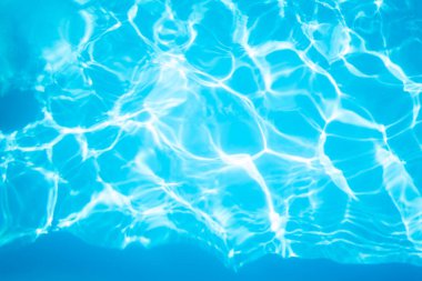 Güneş ışığı berrak mavi su yüzeyinde dans eder, karmaşık desenler oluşturur.