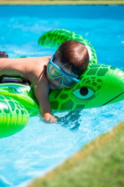 Havuzda yüzen şişme kaplumbağanın üzerinde güneşli yaz gününde gözlük takan bir çocuk.