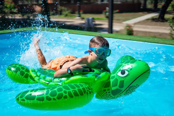Çocuk yüzme havuzunda şişme kaplumbağaya binip yazın tadını çıkarıyor.