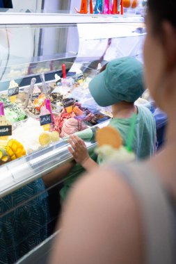 Dondurulmuş vitrinde çeşitli tatlardan dondurma seçen şapkalı genç bir çocuk.