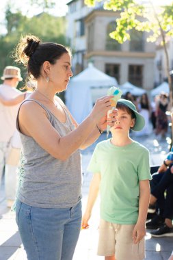 Anne oğlu için dondurma külahı tutuyor güneşli bir yaz gününde şehir ortamında taze tatlı yiyor.