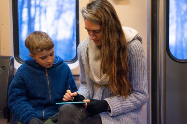 Anne kış boyunca trende seyahat ederken oğluna dijital tablet kullanarak yardım ediyor.
