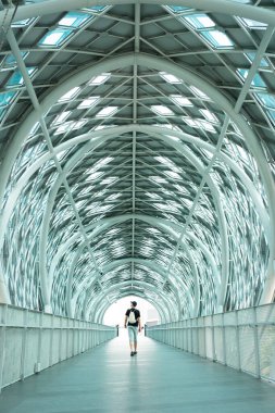 Modern bir yaya köprüsünde kameradan uzaklaşan bir adam.