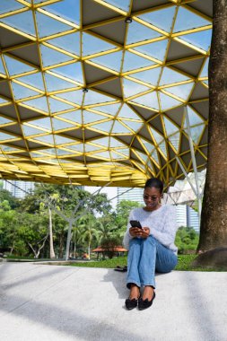 Modern bir şehir parkında akıllı telefon kullanan genç bir kadın.