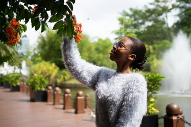 Botanik bahçesindeki portakal çiçeklerini koklayan genç bir kadın çeşmeli bir göletin yanında.