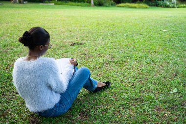 Not defterine not alan genç bir kadın yeşil bir parkın huzurunun tadını çıkarıyor.