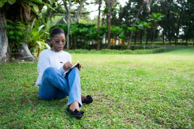 Genç bir kadın, parkın sessizliğinin ve huzurunun tadını çıkarırken defterine not alıyor.