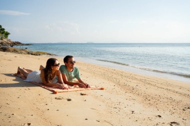 Turistler plaj havlusunda uzanıp tropik plajlarda yaz tatilinin tadını çıkarıyorlar.