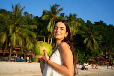 Genç bir kadın tropikal bir sahilde ferahlatıcı bir hindistan cevizinin tadını çıkarıyor.