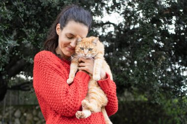 Doğada kızıl kediye sarılan gülümseyen kadın.