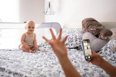 Anne akıllı telefon kullanarak kızının yatağında el sallarken fotoğrafını çekiyor. Doldurulmuş su aygırı oyuncağı.