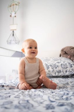 Mutlu bebek yatak odasında bir yatakta oturuyor, gülümsüyor ve başka tarafa bakıyor.