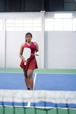 Elinde raket ve top tutan kendine güvenen yankesiciler, kapalı sahada servis yapmaya hazır.