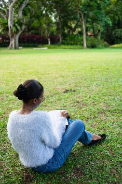 Öğrenci parkta çimlerin üzerinde oturup ders çalışmaktan zevk alıyor.