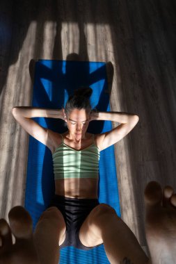 Woman exercising her abdominal muscles doing sit-ups on a blue yoga mat in her living room