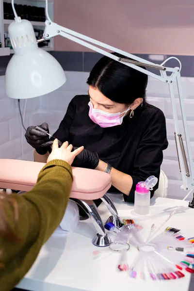 work as a manicurist in a salon, manicurist working at the table wearing black gloves and a mask. Neil beauty salon. Profession manicurist