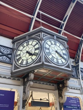 Londra 'nın Paddington İstasyonu' ndaki salonun üzerinde asılı olan çok yönlü tarihi saate odaklanmış bir çekim. Perspektif, simetrik ve detaylı tasarımı vurgulayarak, dört saatin ikisini gösteriyor. Görüntü, saatin benzersiz görüntüsünü yakalar. 