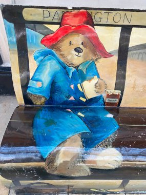 Paddington İstasyonu 'ndaki halka açık bir bankta Paddington Ayısı karakterine odaklanmış duvar resminin yakın çekimi. Resim, elinde bir kavanoz marmelat tutarken klasik mavi spor ceketinin ve kırmızı şapkasının detaylarını vurguluyor.. 