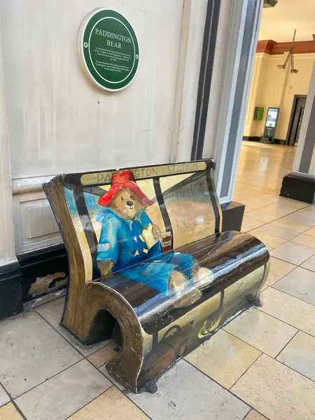 Paddington Bear duvar tablosunun tamamını ve Londra Paddington İstasyonu 'nun etrafını gösteren geniş açılı bir çekim. Bankın eşsiz, kitap benzeri şekli görülebilir. Arkasındaki duvardaki karaktere adanmış bir plaket var.. 