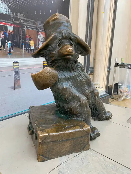 Paddington Ayısı 'nın Londra' daki Paddington İstasyonu 'ndaki bronz heykelinin dörtte üçlük yakın çekimi. Ayı klasik şapkasını takarak bavulunun üzerine oturur ve üzerinde 
