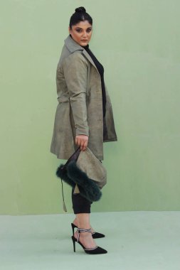 Uzun yeşil ceketli, siyah pantolonlu, kürk şapkalı bir kadın.