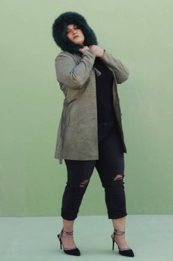 Uzun yeşil ceketli, siyah pantolonlu, kürk şapkalı bir kadın.