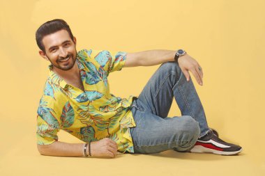 Mavi arka planda çapraz elleri olan sıradan giyinmiş yakışıklı genç bir adamın portresi. Stüdyo çekimi.