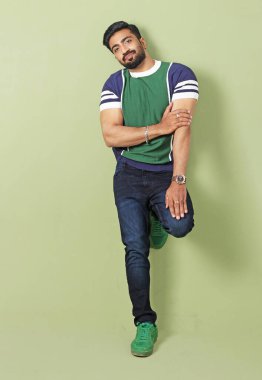 indian young man with crossed legs in casual clothes and jeans posing in studio clipart